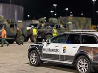 Ein Fahrzeug der Polizei steht vor einem Millitärkonvoi