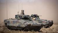 Zwei Panzer vom Typ Puma und Marder fahren durch das Gelände. Im Hintergrund ist viel Staub zu sehen.