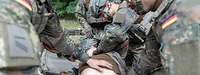 Mehrere Soldaten versorgen einen am Boden liegenden, verwundeten Soldaten bei einer Übung.