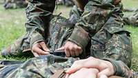 Ein Soldat legt einem verwundeten Soldaten bei einer Übung eine Aderpresse am Oberschenkel an.
