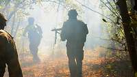 Bewaffnete Soldaten laufen im vernebelten Gelände.