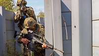 Zwei Soldaten stehen mit Waffen im Anschlag im Graben hinter einer Ecke.