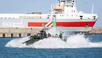 kleines militärisches Eingreifboot mit bewaffneten Soldaten vor einer großen Fähre