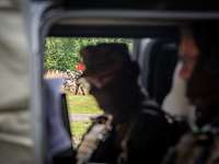 Zwei Soldaten sitzen in einem Fahrzeug mit geöffneter Tür. Draußen laufen weitere Soldaten.