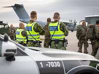 Schwedische Militärpolizisten stehen an ihrem Fahrzeug, im Hintergrund ein militärisches Transportflugzeug