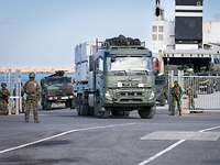 Ein schwedischer Militär-LKW fährt durch einen Hafen, ihm folgen deutsche Fahrzeuge. Soldaten sichern an der Seite