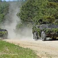 Zwei mit Grünzeug getarnte Militärfahrzeuge fahren über Sandboden