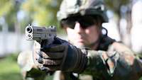 Ein Soldat hält eine Pistole P13 in den Händen vor sich.