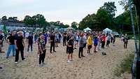 Viele jungen Männer und Frauen stehen in Reihen auf einer Sandfläche.