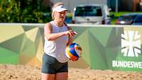 Eine junge Frau steht auf einer Sandfläche und hält einen Volleyball in der Hand.
