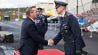 Zwei Männer begrüßen sich lächelnd per Handschlag, eine trägt eine militärische Uniform.