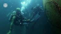 Mehrere Kampfschwimmer tauchen neben einer Kugel. 