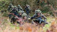 Eine Gruppe von Soldaten bewegt sich in einem Wiesengelände.