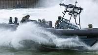 Soldaten fahren in einem Schlauchboot über ein Gewässer. Wasser spritzt hoch.