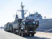 Zwei Militär-Lkw stehen hintereinander vor einem militärischen Schiff