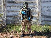 Bewaffneter Soldat in voller Schutzkleidung mit Maske steht vor einer Mauer