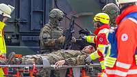 Rettungssanitäter kümmern sich um einen verletzten Soldaten auf einer Trage bei einer Übung.