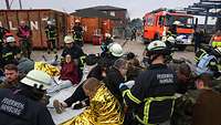 Bei einer Übung werden Verletzte von Feuerwehrleuten und Soldaten an einem Sammelplatz behandelt.