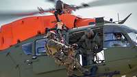 Ein Soldat in einem fliegenden Hubschrauber lässt einen Soldaten mit Hund an der Winde ab.