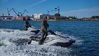 Zwei Soldaten auf zwei Wasserfahrzeugen auf dem Wasser vor der Werft