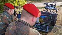 Zwei Soldaten an Bildschirmen; im Hintergrund steht ein vierbeiniger Roboter.