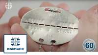 Eine Hand hält eine Metallmarke mit Stanzung, davor das Bundeswehr-Logo links in einem Kasten