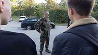 Ein Soldat im Feldanzug spricht im Freien mit zwei Männern in ziviler Kleidung.