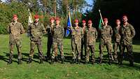 Zehn Soldaten stehen als lockere Gruppe, hinter drei Soldaten steht je ein Wimpel ihrer Batterie.
