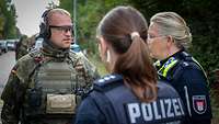 Ein Soldat und zwei Polizistinnen auf einer Straße im Gespräch.