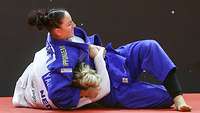 Zwei Frauen in blauen und weißen Judoanzügen kämpfen am Boden.