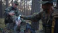 Ein Soldat schüttet Fußpuder auf den nackten Fuß eines Kameraden, der auf seinem Rucksack sitzt.