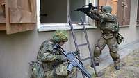 Ein Soldat kniet an einer Leiter, während ein anderer ins Gebäude schießt.