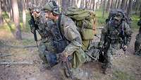 Vier Soldaten tragen einen Verwundeten auf einem Tragetuch durch einen Nadelwald.