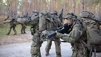 In verschiedene Richtungen sichernd überwinden Soldaten paarweise einen Weg auf der Waldkampfbahn.