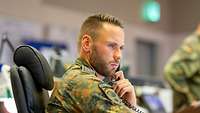 Soldiers sitting in a situation centre in front of computer monitors watching a screen