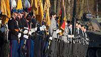 Niederländische Soldaten in Paradeuniform und deutsche Soldaten stehen mit Flaggen nebeneinander.