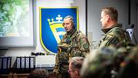 Ein Soldat vor einer Leinwand weist seine Soldaten in die nun zu treffenden Maßnahmen ein.