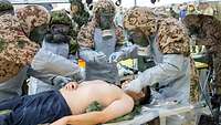 Soldaten verschiedener Nationen mit ABC-Schutzausstattung behandeln einen Patienten