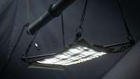 Eine Lampe, in Form eines Lichteppichs, ist mit Bändern an einer schwarzen Metallstange befestigt