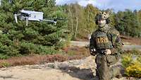 Ein Soldat kniet im Gelände und steuert eine Drohne vom Typ Autel.