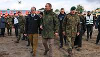 Drei Männer, zwei davon in Flecktarnuniform, laufen nebeneinander und sprechen miteinander.