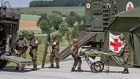 Medical forces provide medical care to a patient on a stretcher. Medical vehicle, mobile aid station with tent.