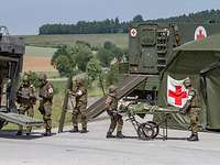 Exercise: Medical evacuation to a mobile aid station (Role 1) Medical forces provide medical care to a patient on a stretcher. Medical vehicle, mobile aid station with tent.