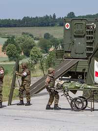 Exercise: Medical evacuation to a mobile aid station (Role 1) Medical forces provide medical care to a patient on a stretcher. Medical vehicle, mobile aid station with tent.