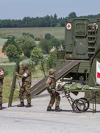 Medical forces provide medical care to a patient on a stretcher. Medical vehicle, mobile aid station with tent.