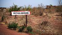 Ein rot umrandetes, weißes Ortsschild mit der schwarzen Aufschrift „Koulikoro“