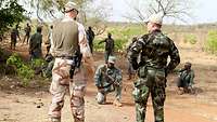 Ein irischer und ein schwedischer Soldat stehen vor malischen Soldaten im Gelände
