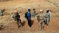 Zwei deutsche Soldaten sprechen mit einem malischen Soldaten, im Hintergrund liegen malische Soldaten in Stellung