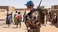 Soldat mit Funkgerät auf Fußpatrouille, malische Kinder im Hintergrund
