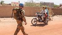 Deutscher Soldat auf Fußpatrouille, zwei Malier auf einem Roller fahren vorbei